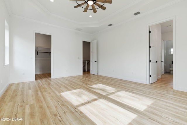 unfurnished bedroom featuring light hardwood / wood-style flooring, ceiling fan, crown molding, a tray ceiling, and a spacious closet