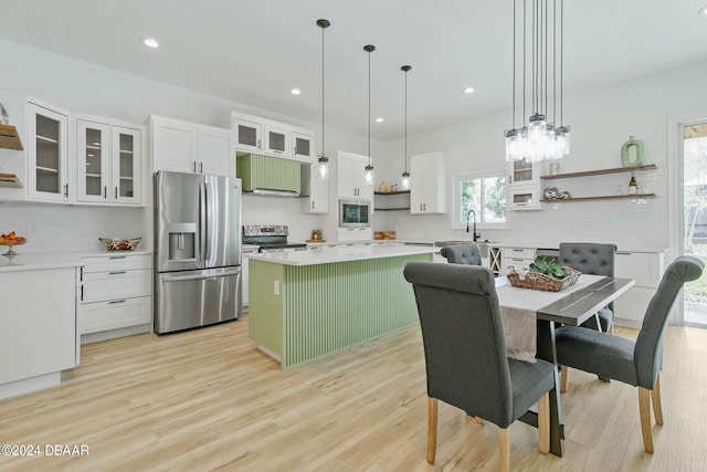 kitchen featuring stainless steel appliances, white cabinetry, hanging light fixtures, a center island, and light wood-type flooring