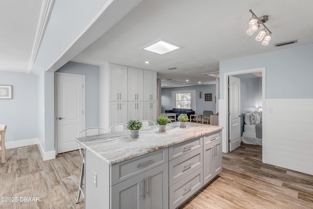 kitchen featuring a kitchen bar, light hardwood / wood-style floors, light stone counters, and a center island