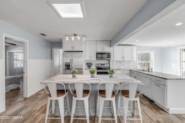 kitchen with stainless steel appliances, a center island, white cabinetry, and sink