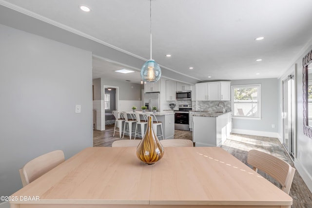 dining space featuring lofted ceiling, sink, crown molding, and light hardwood / wood-style flooring