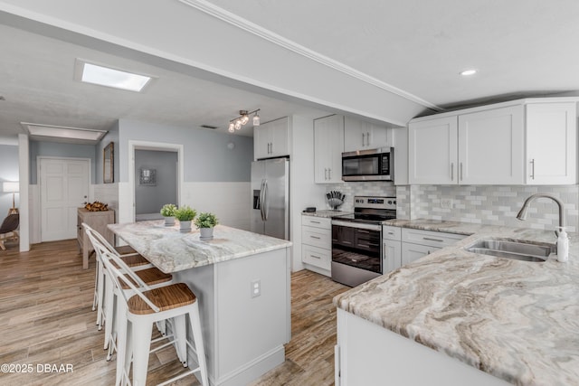 kitchen featuring a center island, sink, white cabinetry, light stone countertops, and stainless steel appliances