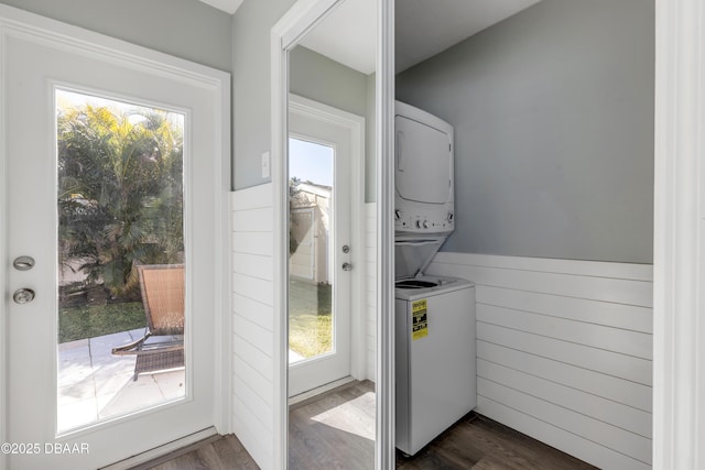 laundry area with dark wood-type flooring, stacked washer / drying machine, and plenty of natural light