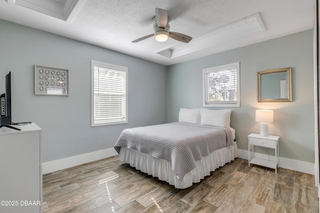 bedroom with a raised ceiling, ceiling fan, light wood-type flooring, and a textured ceiling