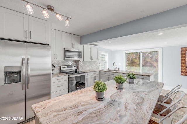 kitchen with white cabinetry, stainless steel appliances, a kitchen breakfast bar, light stone counters, and sink