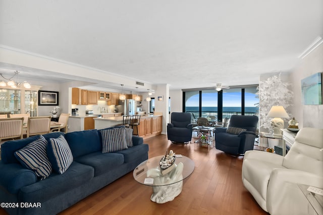 living room featuring ceiling fan with notable chandelier, dark hardwood / wood-style flooring, a water view, floor to ceiling windows, and crown molding