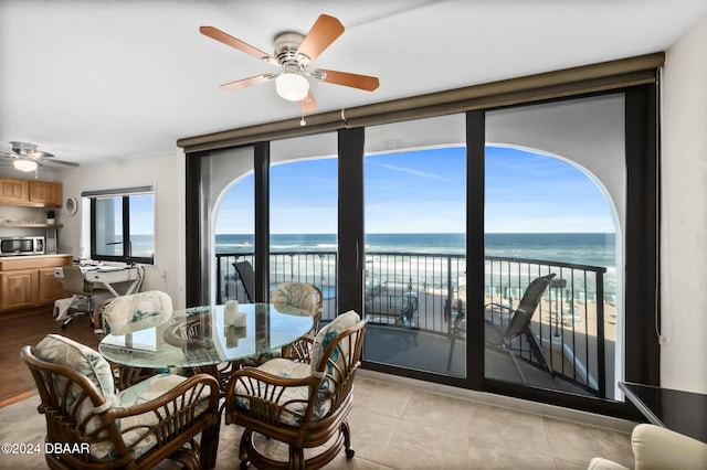 dining room featuring a beach view, a water view, light tile patterned floors, and ceiling fan