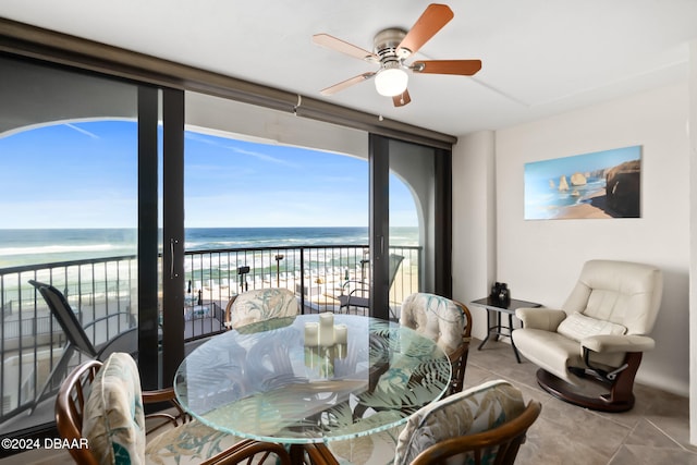 interior space featuring light tile patterned floors, a water view, a view of the beach, and ceiling fan