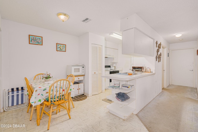 kitchen featuring kitchen peninsula, light carpet, white microwave, exhaust hood, and white cabinetry