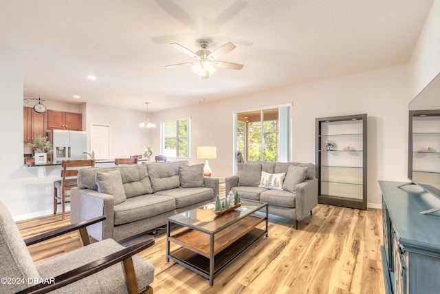 living room with a textured ceiling, light hardwood / wood-style floors, and ceiling fan with notable chandelier