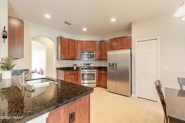 kitchen featuring kitchen peninsula, a textured ceiling, stainless steel appliances, sink, and dark stone countertops