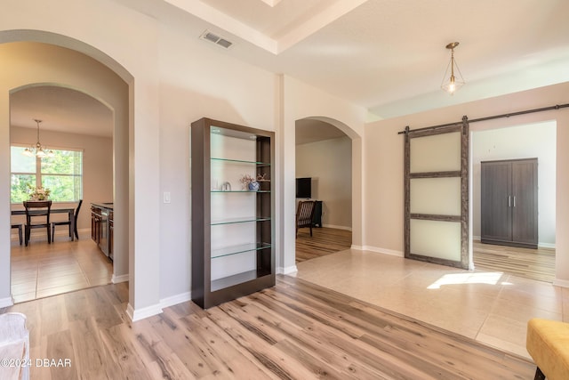 spare room featuring a barn door, light hardwood / wood-style flooring, and a chandelier