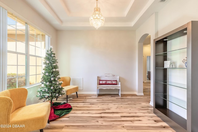 sitting room featuring a tray ceiling, a wealth of natural light, a notable chandelier, and light wood-type flooring