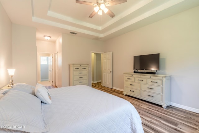 bedroom with ceiling fan, a raised ceiling, and light hardwood / wood-style flooring