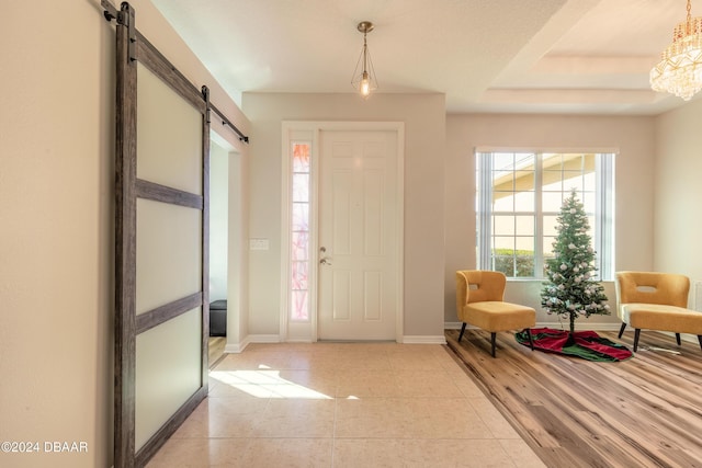 entrance foyer with a raised ceiling, a barn door, and light wood-type flooring