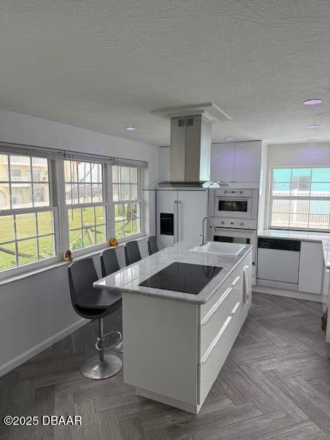 kitchen featuring white appliances, white cabinetry, island range hood, an island with sink, and a textured ceiling