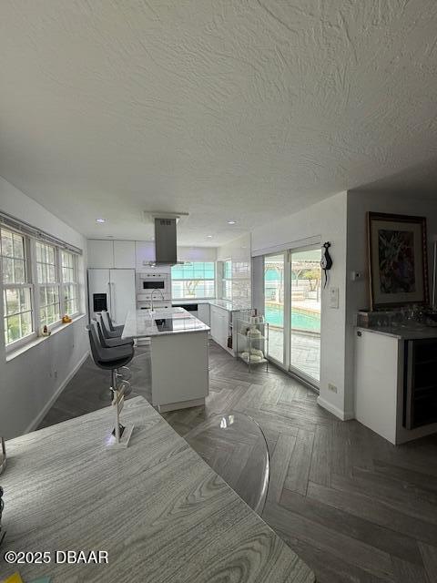 interior space featuring built in refrigerator, a center island, extractor fan, white cabinets, and parquet floors