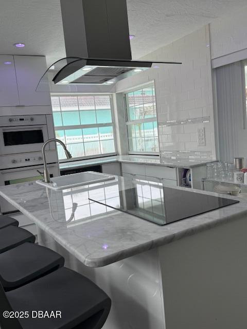 kitchen featuring light stone counters, island exhaust hood, sink, and white oven