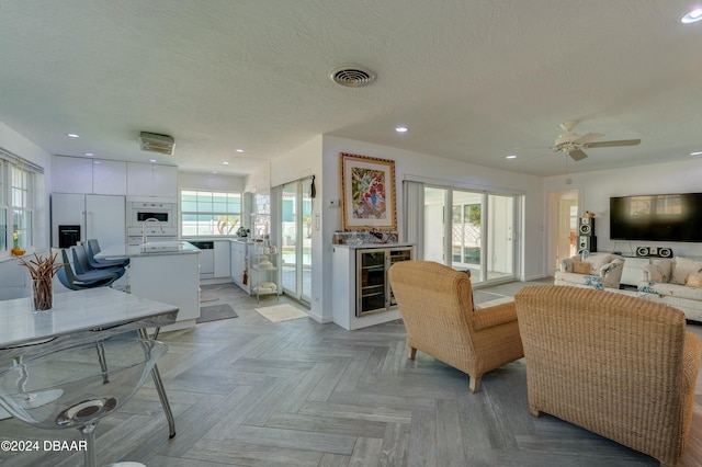 living room with beverage cooler, a wealth of natural light, a textured ceiling, and light parquet floors