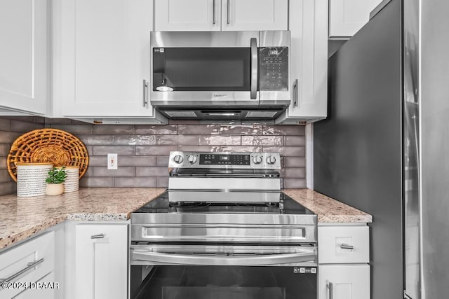 kitchen featuring tasteful backsplash, white cabinets, appliances with stainless steel finishes, and light stone countertops