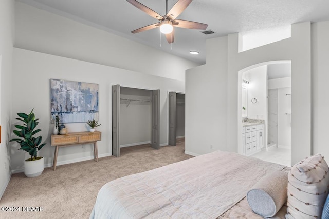 bedroom with multiple closets, ensuite bathroom, arched walkways, baseboards, and light colored carpet