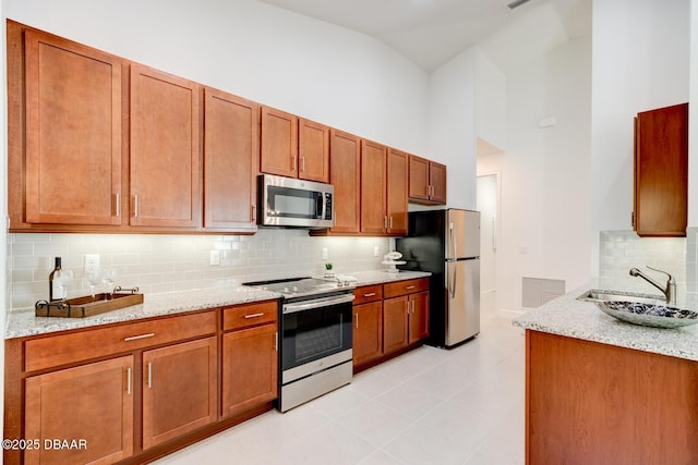 kitchen featuring sink, stainless steel appliances, high vaulted ceiling, light stone counters, and tasteful backsplash