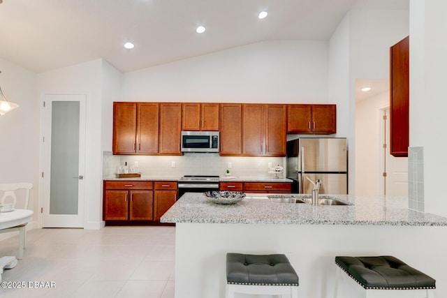 kitchen featuring light stone counters, sink, stainless steel appliances, and a breakfast bar