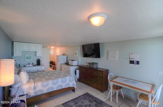 bedroom with a textured ceiling, white fridge, and light tile patterned floors