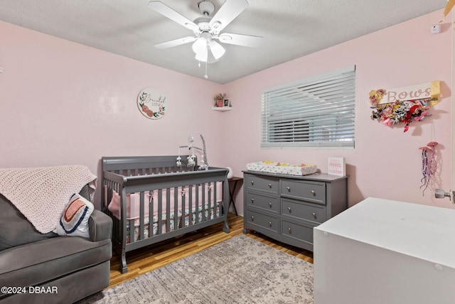 bedroom featuring a textured ceiling, ceiling fan, a crib, and light wood-type flooring