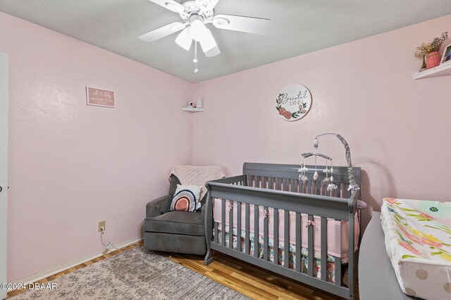 bedroom featuring a crib, light wood-type flooring, and ceiling fan