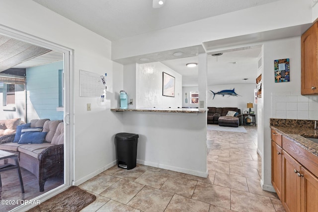 kitchen with stone counters, light tile patterned floors, tasteful backsplash, and kitchen peninsula