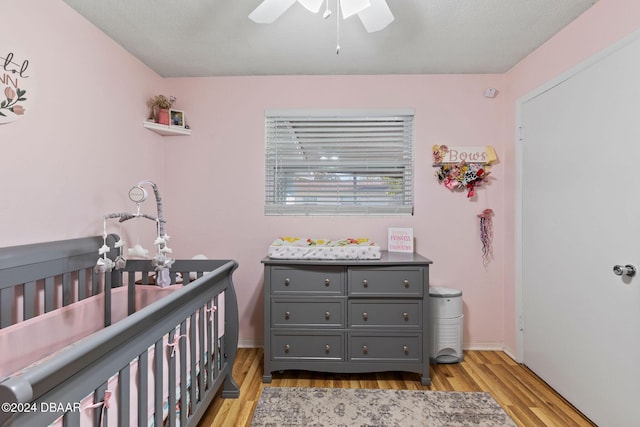 bedroom with a nursery area, a textured ceiling, light hardwood / wood-style flooring, and ceiling fan