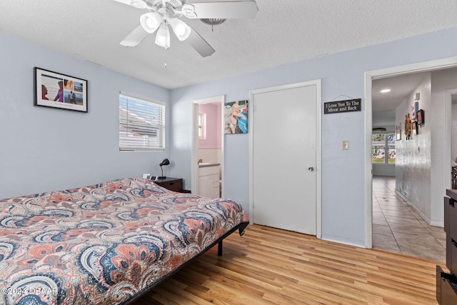 bedroom with ensuite bathroom, light hardwood / wood-style flooring, ceiling fan, and a textured ceiling