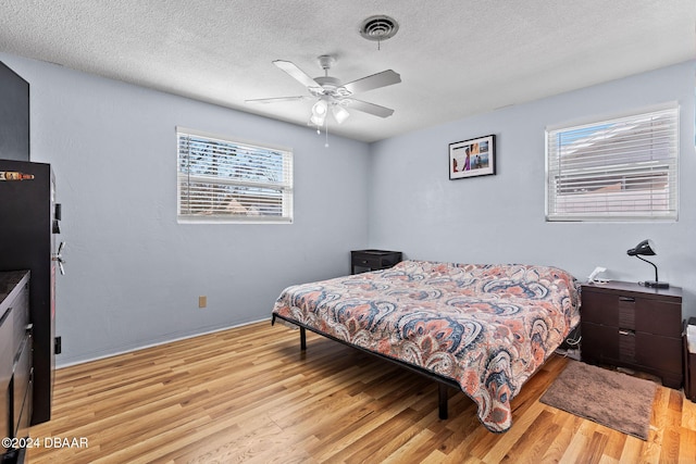 bedroom featuring black refrigerator, a textured ceiling, light wood-type flooring, and ceiling fan