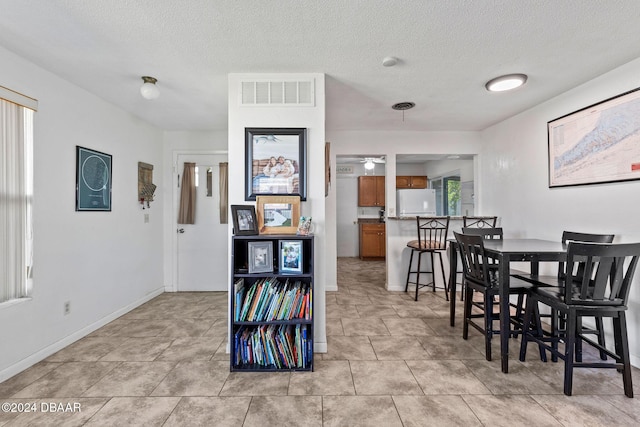 tiled dining space with ceiling fan, a healthy amount of sunlight, and a textured ceiling