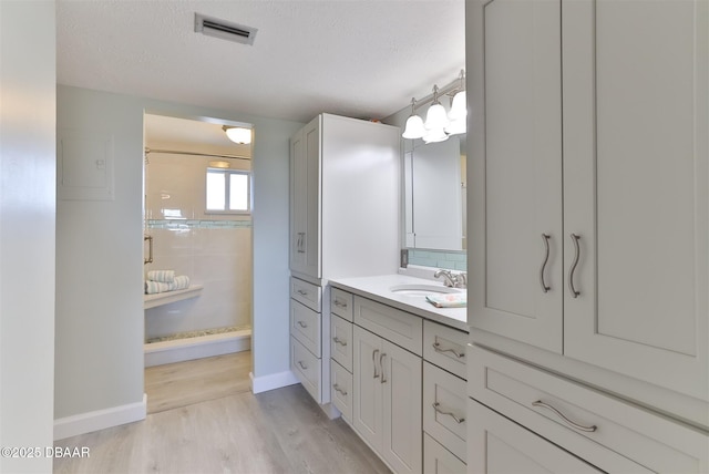 bathroom featuring a textured ceiling, wood finished floors, vanity, visible vents, and tiled shower