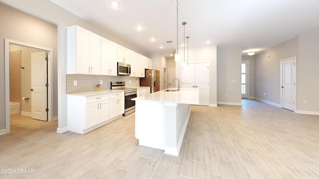 kitchen with hanging light fixtures, light hardwood / wood-style floors, a center island with sink, white cabinets, and appliances with stainless steel finishes