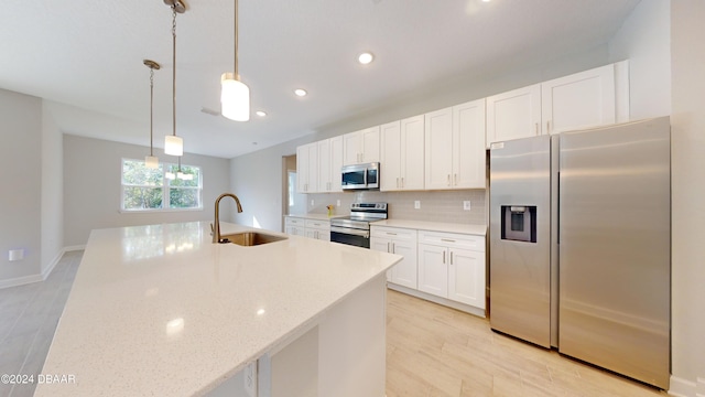 kitchen featuring light stone counters, stainless steel appliances, sink, white cabinets, and hanging light fixtures