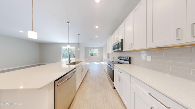 kitchen with pendant lighting, sink, light wood-type flooring, white cabinetry, and stainless steel appliances