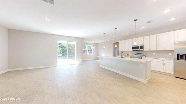 kitchen featuring stainless steel appliances, decorative light fixtures, light hardwood / wood-style flooring, white cabinets, and an island with sink