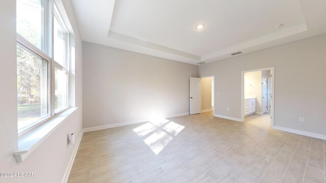 spare room featuring light wood-type flooring, a tray ceiling, and a healthy amount of sunlight