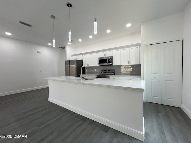 kitchen featuring decorative backsplash, a large island with sink, stainless steel appliances, white cabinetry, and a sink