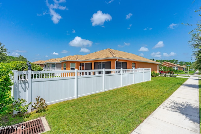 view of side of property with a sunroom, a tile roof, fence, and a lawn