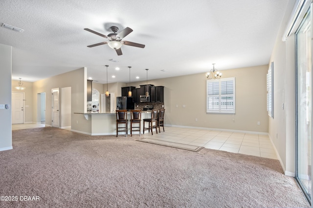 unfurnished living room with light colored carpet, visible vents, light tile patterned flooring, a textured ceiling, and ceiling fan with notable chandelier