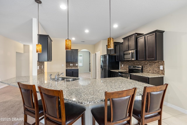 kitchen with light stone counters, arched walkways, appliances with stainless steel finishes, a sink, and a peninsula