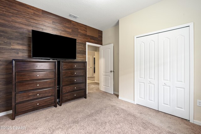 unfurnished bedroom with a closet, visible vents, light carpet, a textured ceiling, and baseboards