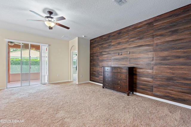 unfurnished living room featuring arched walkways, a textured ceiling, wood walls, visible vents, and carpet