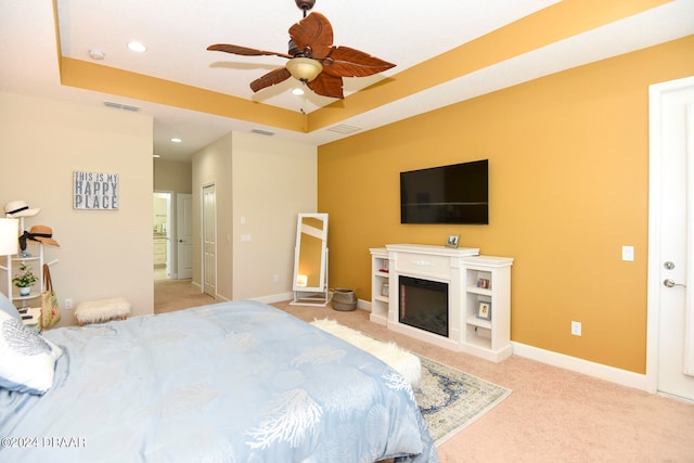 bedroom with light carpet, ceiling fan, and a raised ceiling