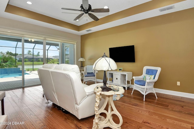 living room with hardwood / wood-style flooring, ceiling fan, and a raised ceiling