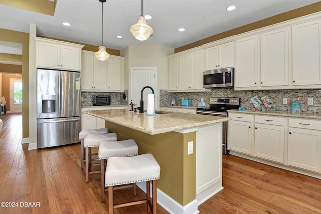 kitchen featuring stainless steel appliances, an island with sink, light wood-type flooring, and tasteful backsplash